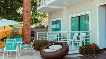 An outdoor seating area with wicker chairs and a round wicker sofa, a white balcony railing, and a yellow umbrella.