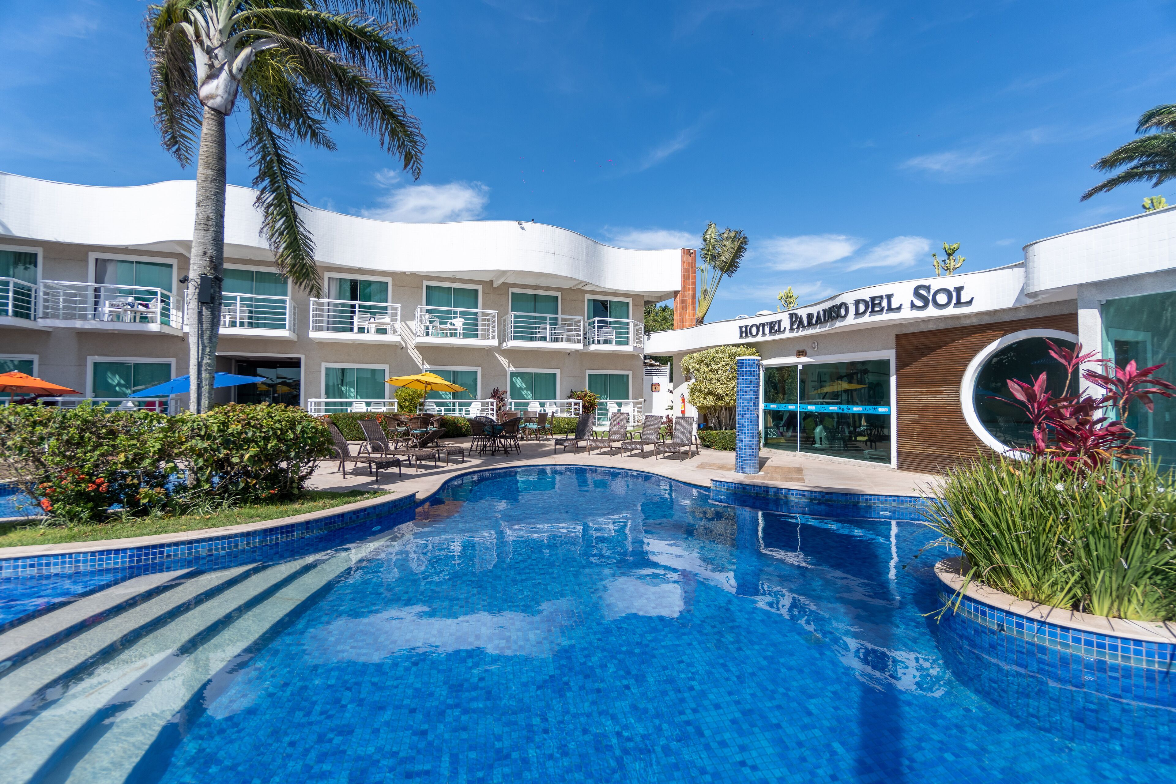 A hotel with a swimming pool, outdoor seating, and a palm tree.