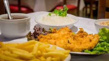A table with a plate of fried fish, a bowl of rice, a bowl of soup, and a plate of fries.