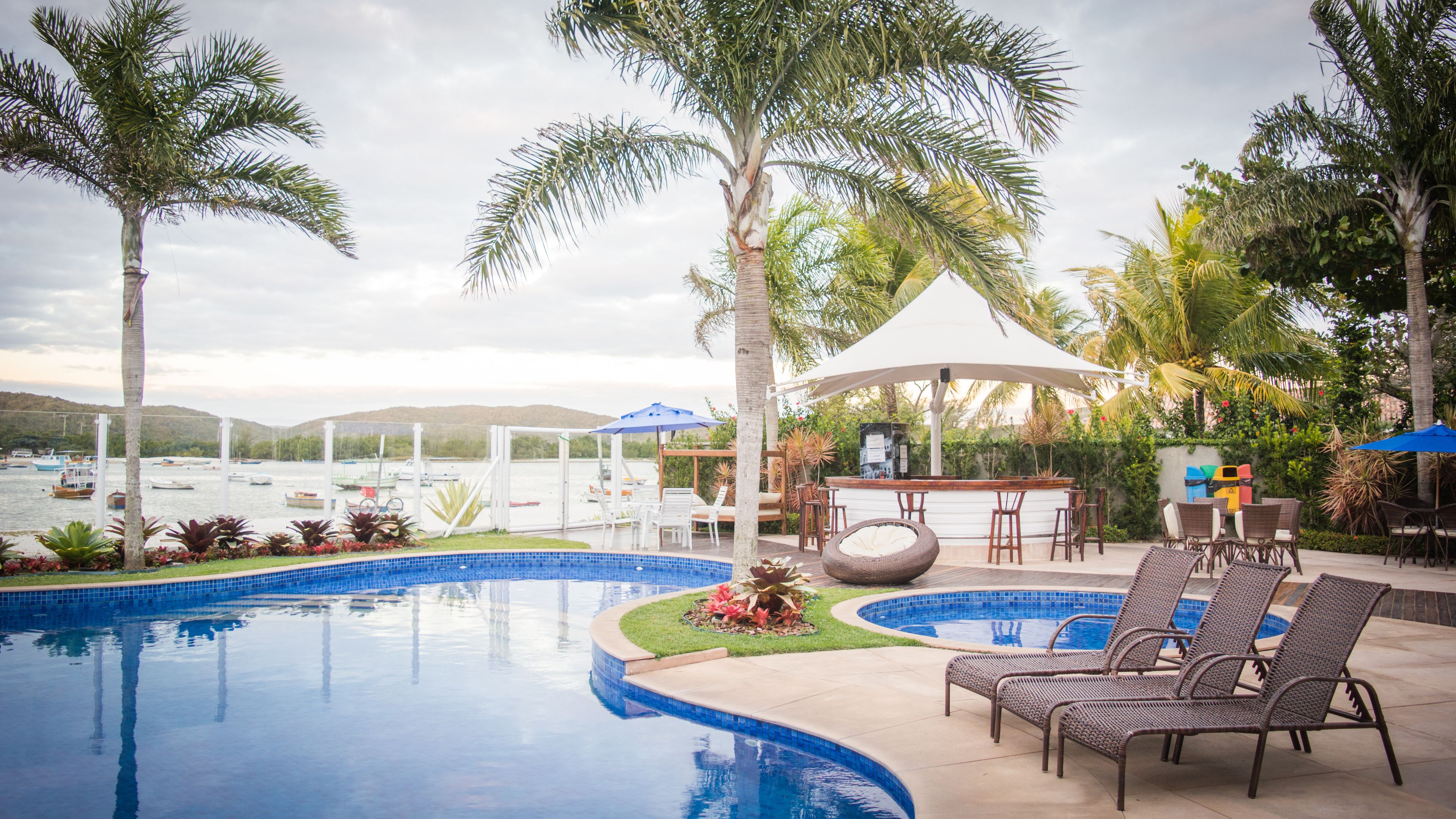A swimming pool with lounge chairs and a bar area, surrounded by palm trees and a view of the water.