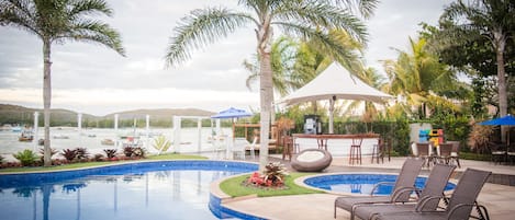 A swimming pool with lounge chairs and a bar area, surrounded by palm trees and a view of the water.