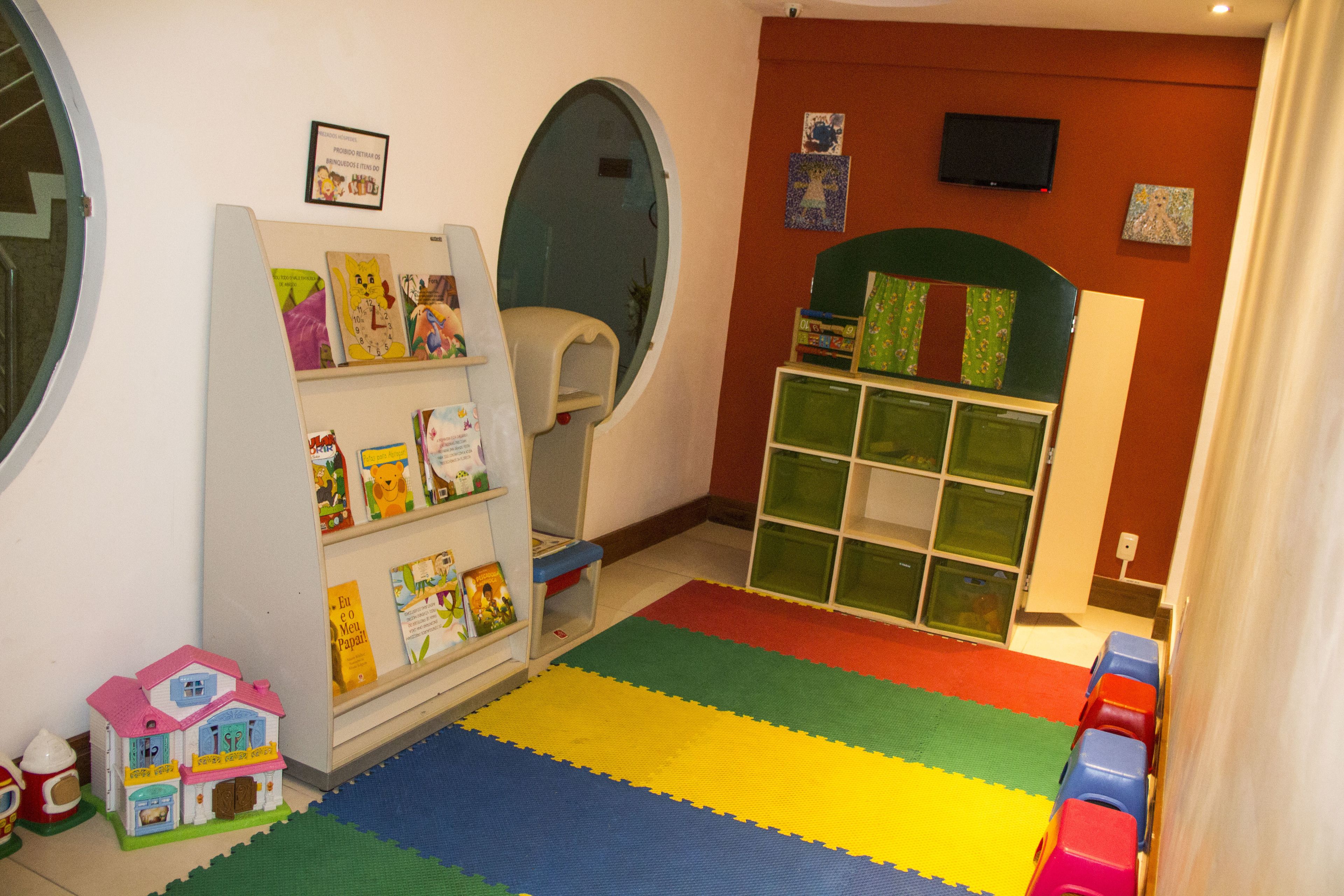 Une salle de jeux pour enfants avec une bibliothèque, des tapis de jeu colorés et un train jouet.