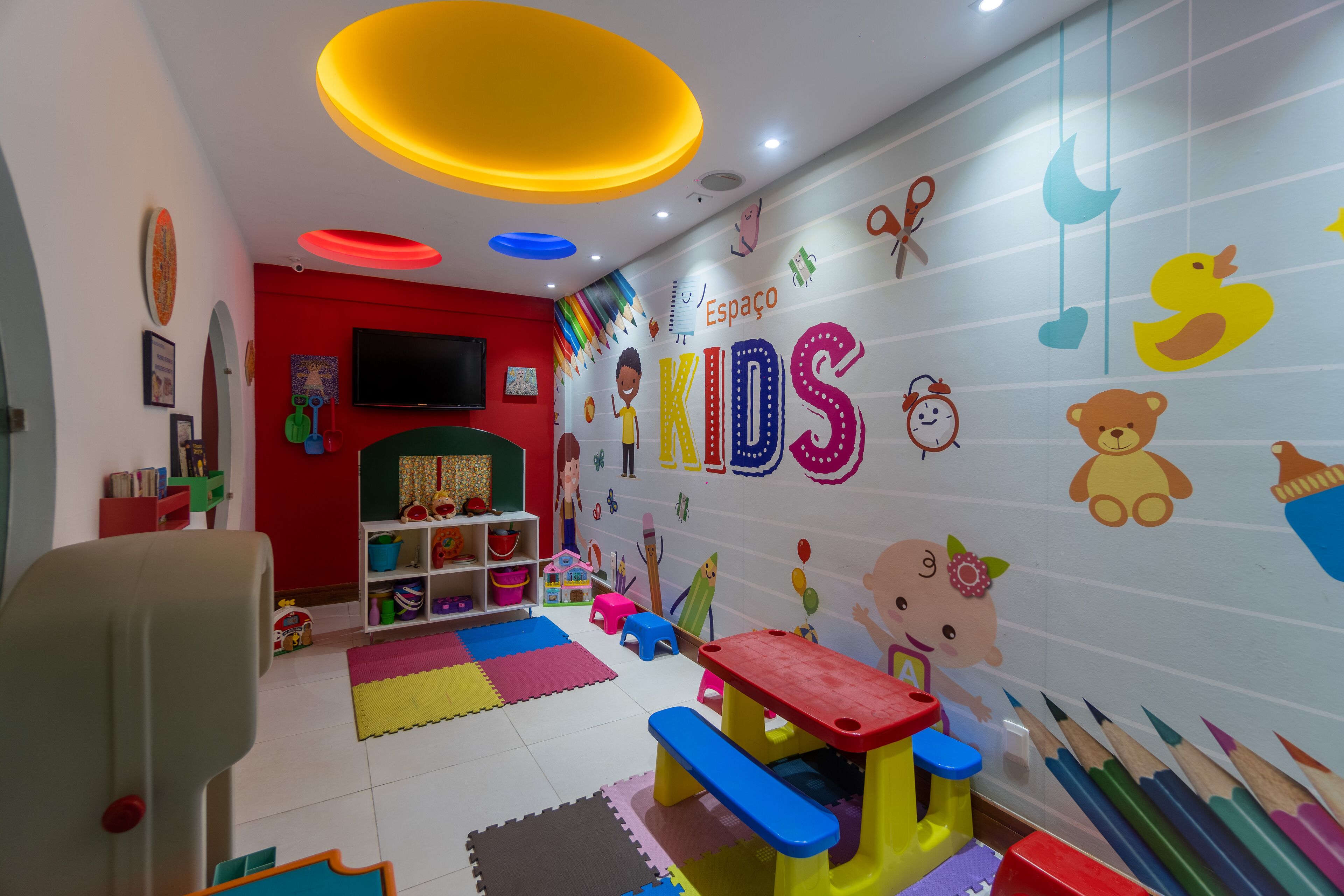 Uma sala de jogos infantil com mobiliário colorido, brinquedos educativos e decorações nas paredes.