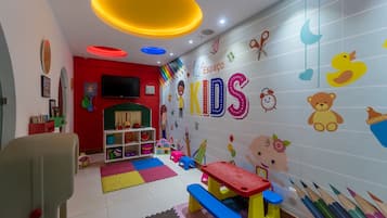 Uma sala de jogos infantil com mobiliário colorido, brinquedos educativos e decorações nas paredes.