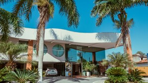Un edificio moderno con fachada curva, palmeras y un coche estacionado al frente.