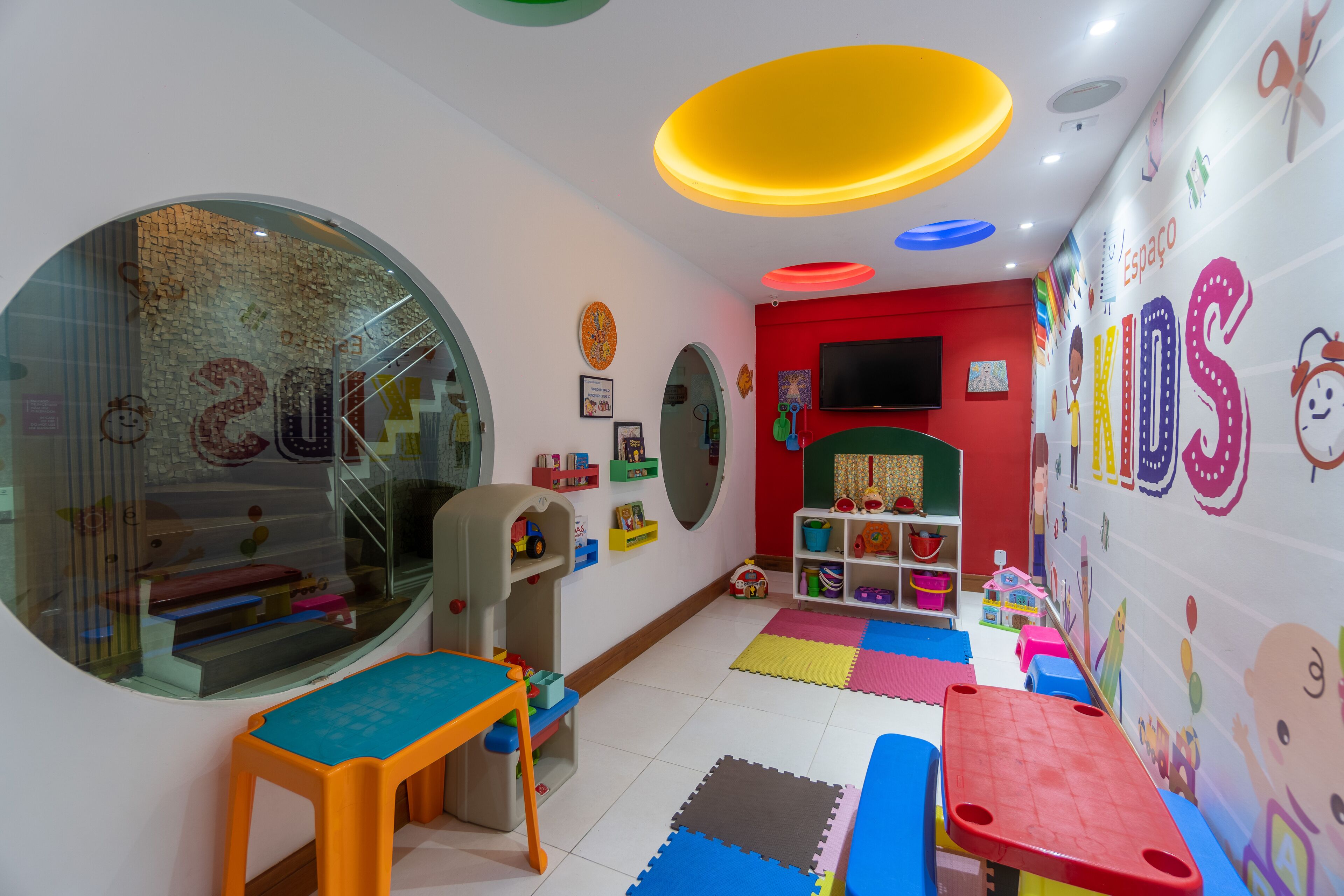 Une salle de jeux pour enfants avec des tapis de jeu colorés, des jouets et des décorations murales à vocation éducative.