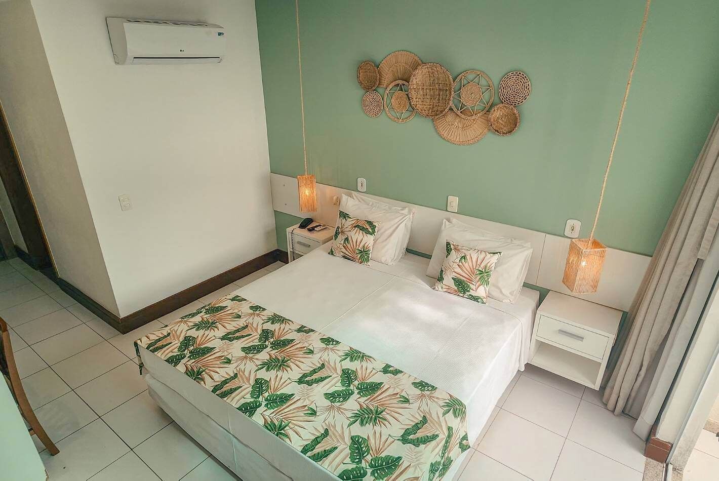 A bedroom with a bed, nightstands, a wall-mounted air conditioner, and a decorative wall hanging.