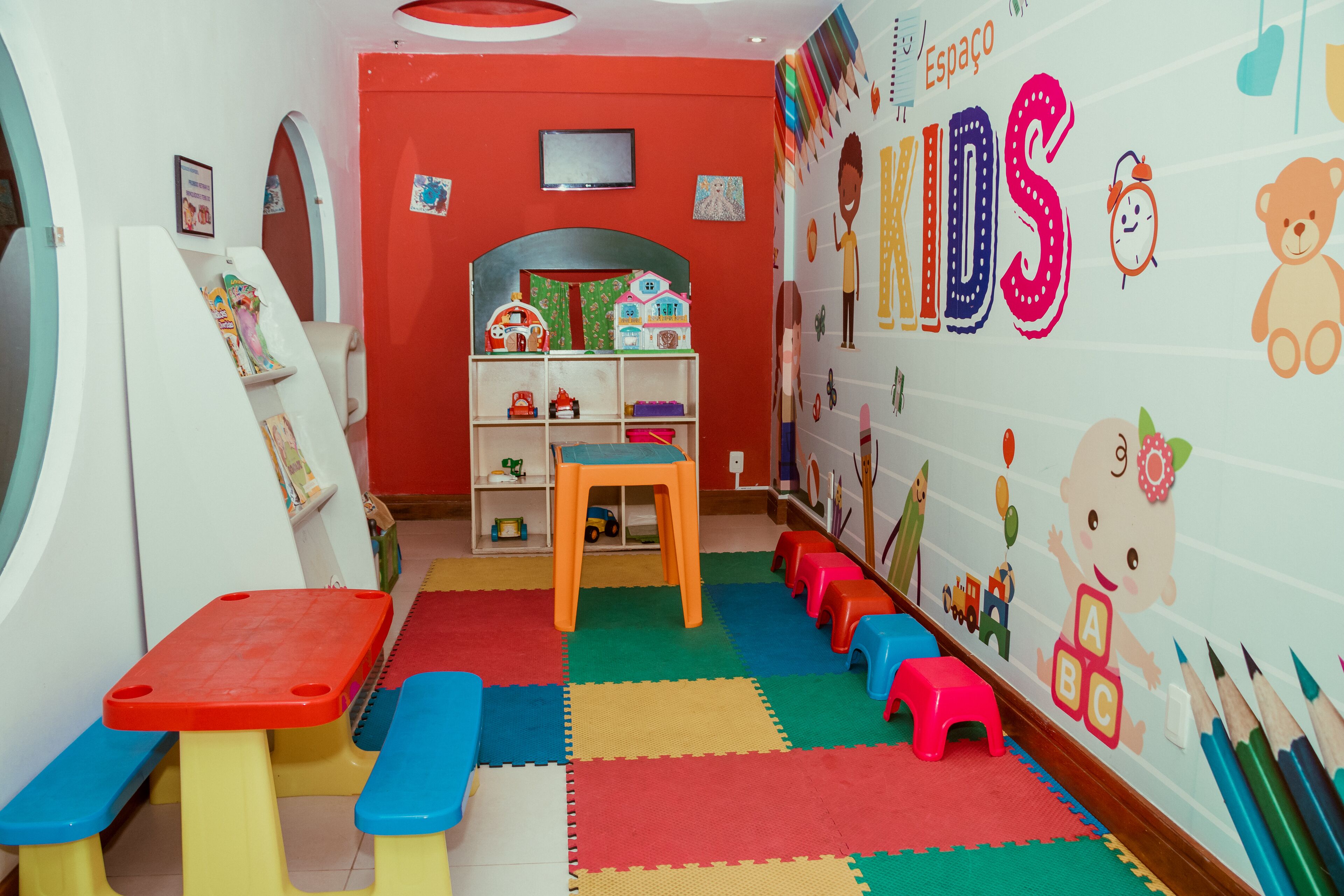 Une salle de jeux pour enfants avec des tapis colorés, une petite table et des jouets.