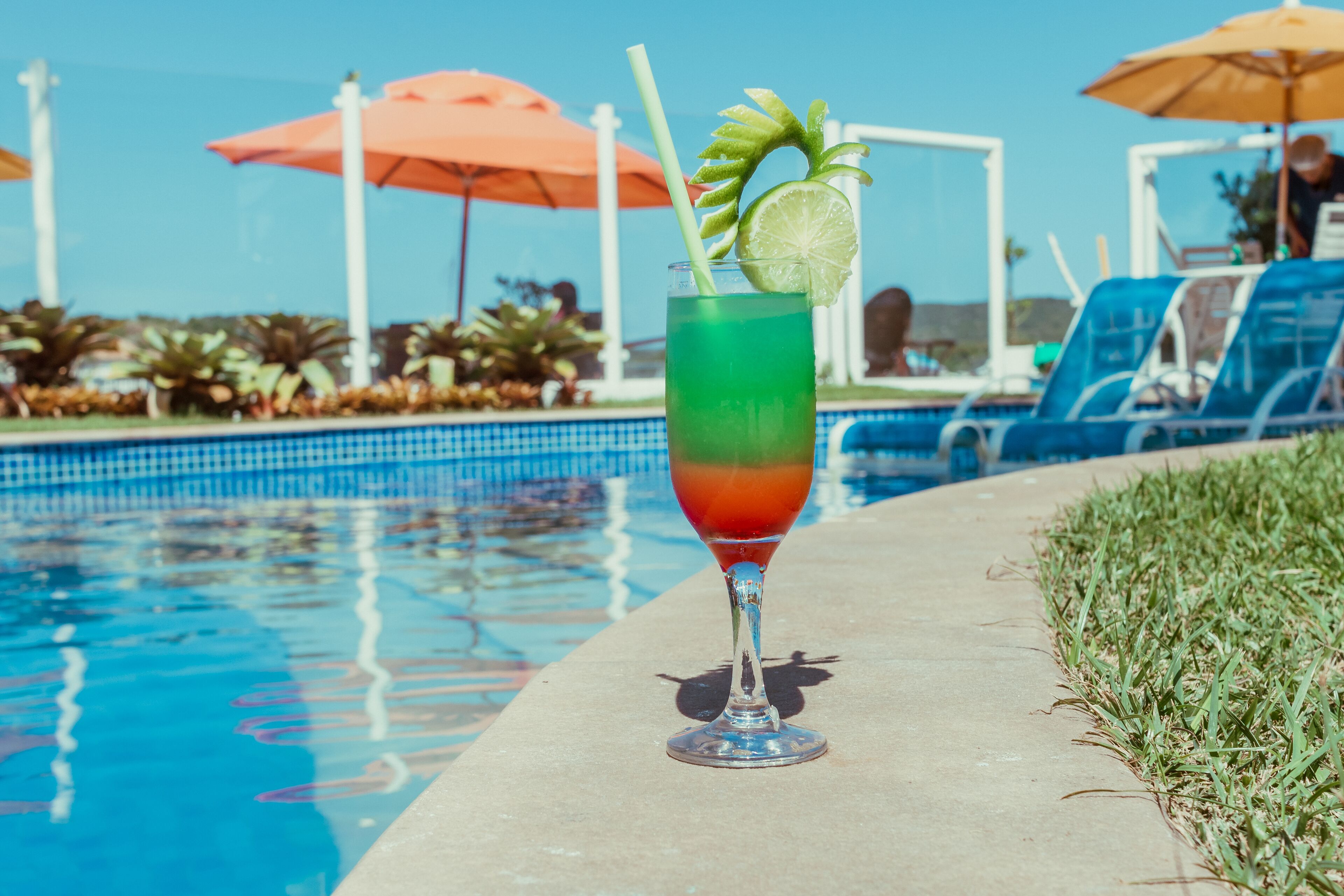 A poolside setting with a clear view of the pool, lounge chairs, and umbrellas.