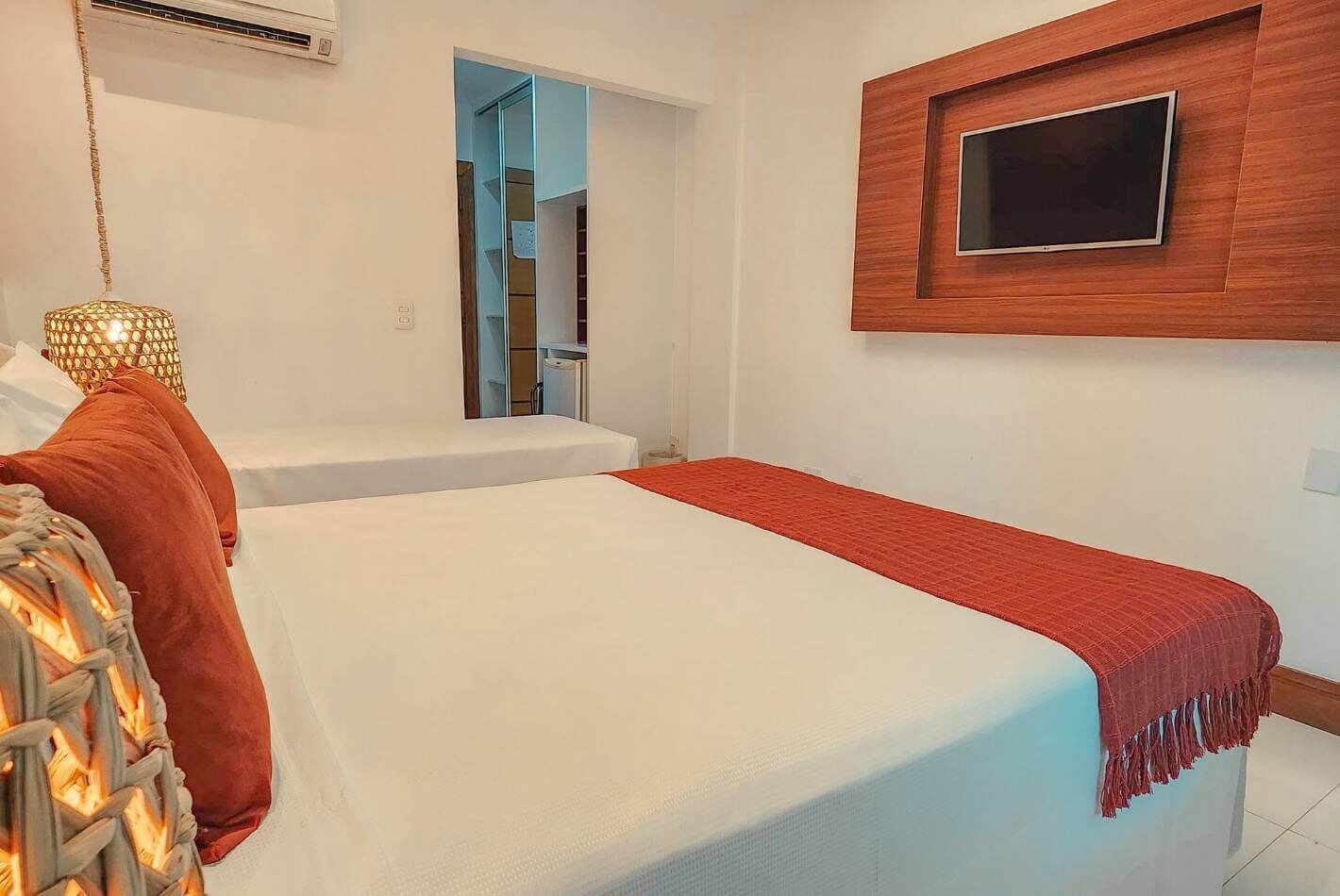 Una habitación de hotel con dos camas, un televisor montado en la pared y una lámpara de fibras naturales.