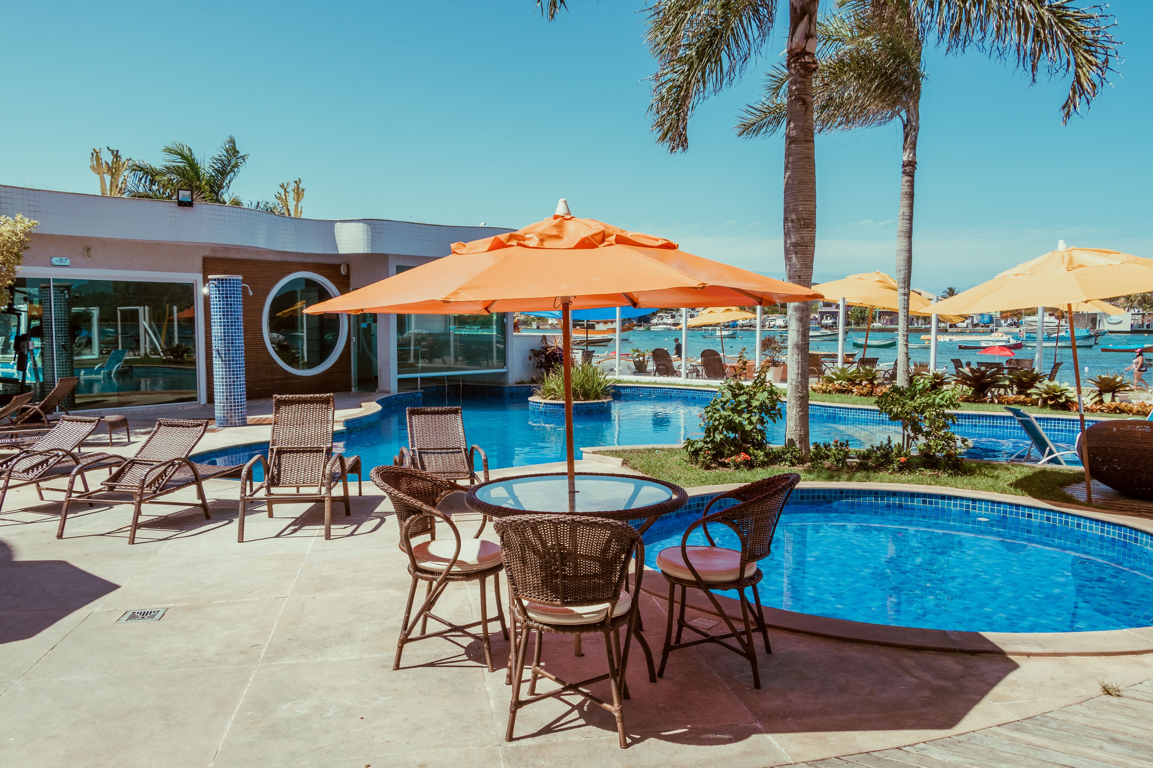 A pool area with lounge chairs and umbrellas, surrounded by palm trees and a clear blue sky.