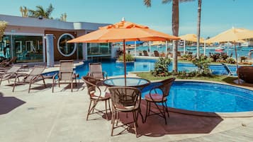 A pool area with lounge chairs and umbrellas, surrounded by palm trees and a clear blue sky.