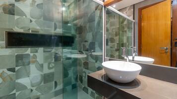 A modern bathroom with a glass shower enclosure, a white sink, and a wooden door.