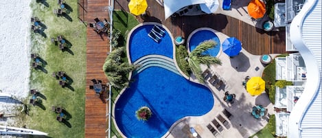 Una gran piscina al aire libre con varias secciones, rodeada de sillones de descanso y sombrillas.
