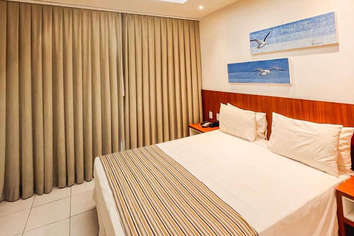 Una habitación de hotel con una cama grande, una mesita de noche, una lámpara de techo y dos obras de arte en la pared.