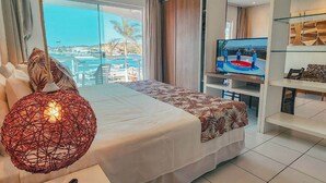 Habitación de hotel moderna con una cama grande, televisor y vistas al mar.
