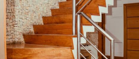 Una escalera con escalones de madera y barandillas de metal, que conduce a una habitación con pared de piedra y puerta de madera.