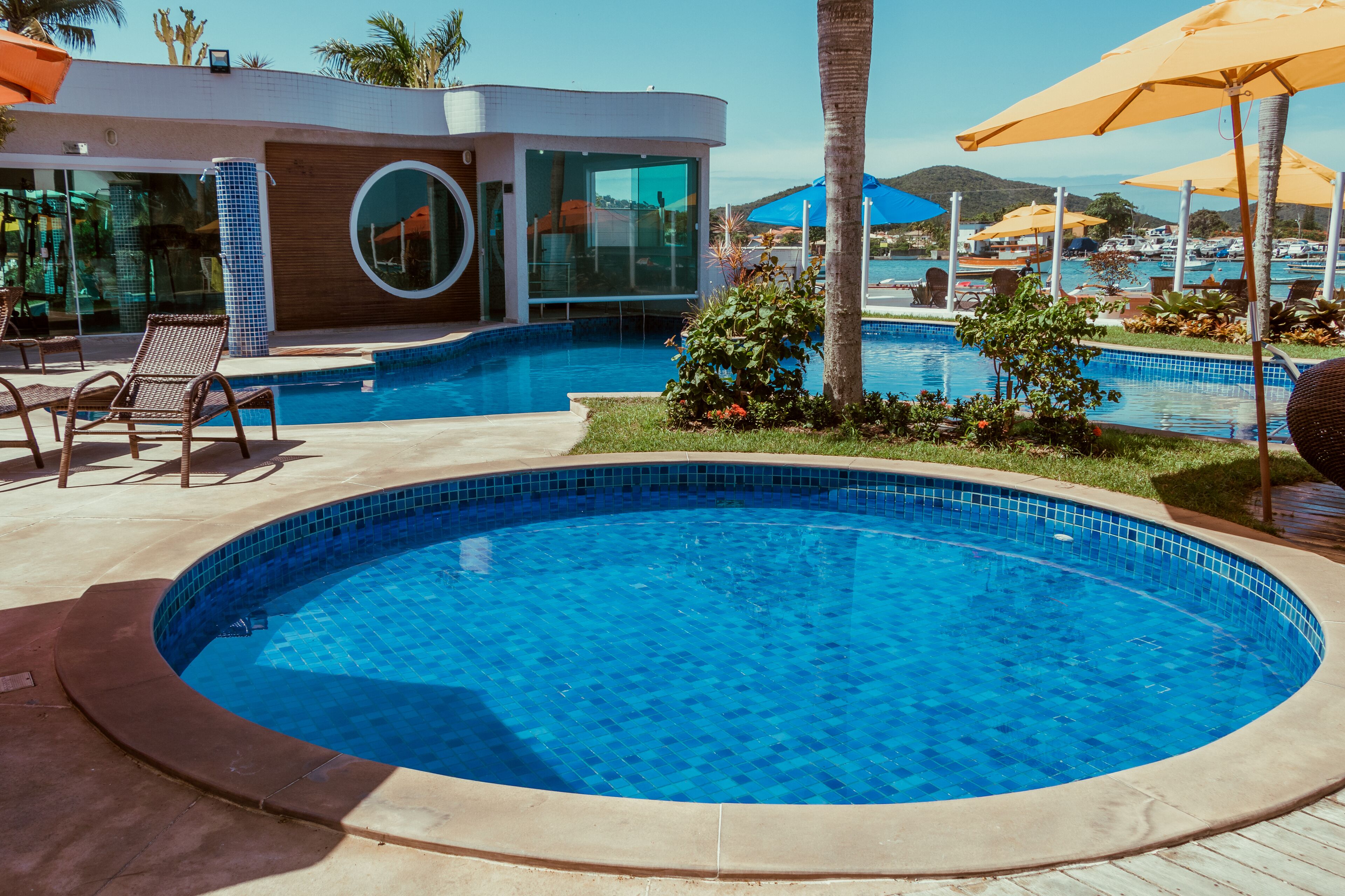A modern pool area with a large circular pool, lounge chairs, and umbrellas.