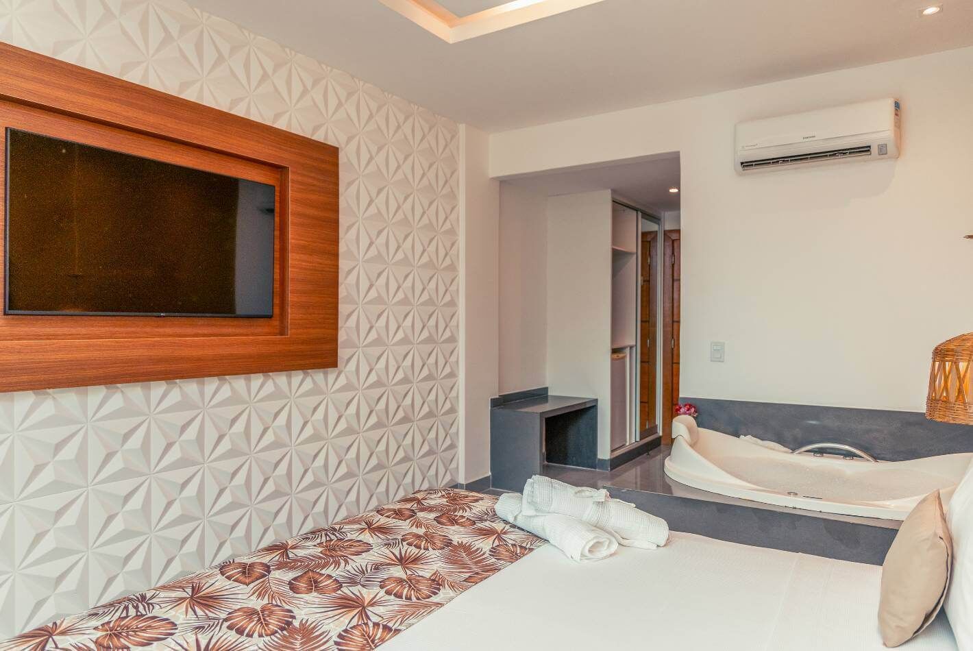 Una habitación de hotel moderna con una pared de diseño geométrico, un ventanal grande, una cama con colcha estampada, una mesita de noche y un equipo de aire acondicionado.