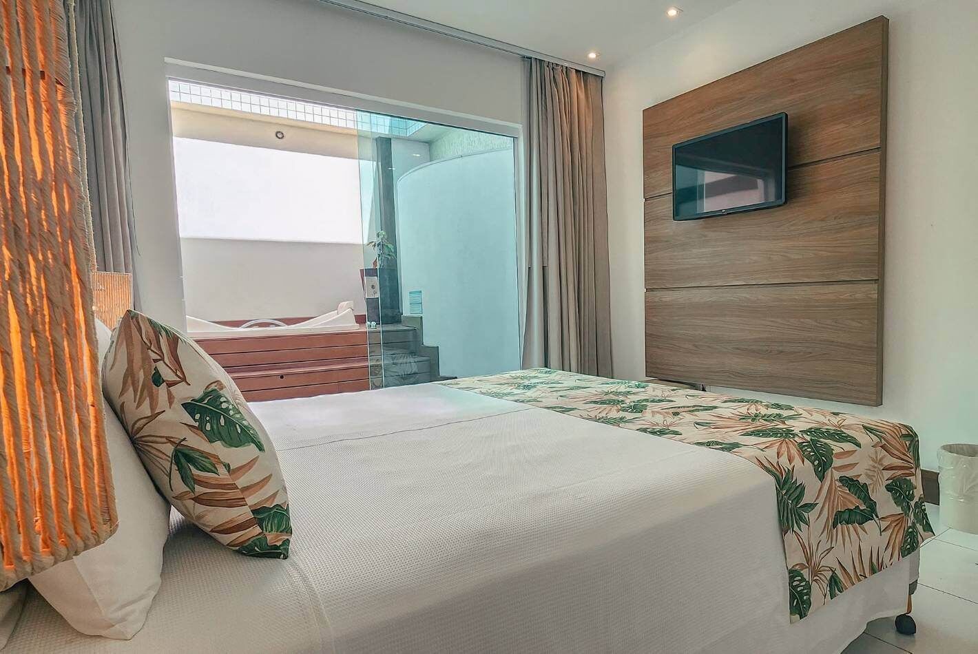 Un dormitorio moderno con cama, televisor montado en un panel de madera y balcón con cortinas.