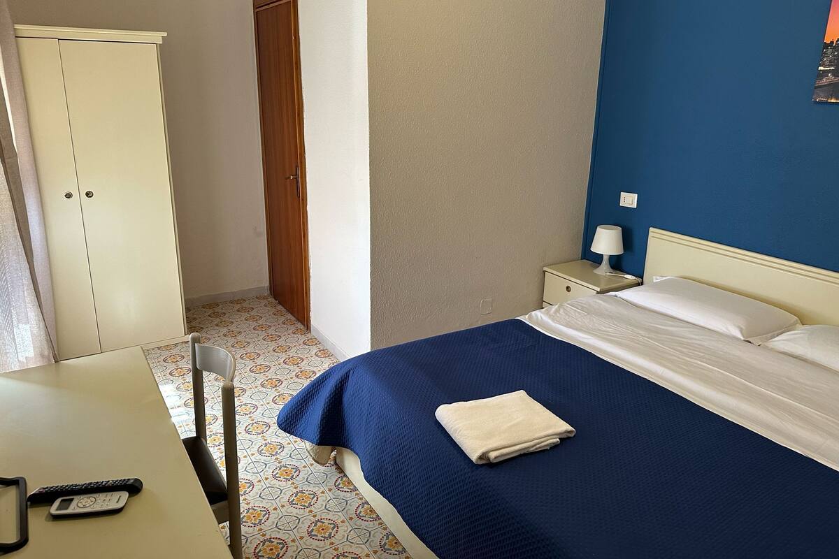 Une chambre d’hôtel comprenant un lit, un bureau, une chaise, une armoire et une table de chevet avec une lampe.