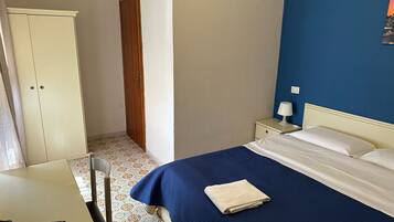 Een hotelkamer met een bed, een bureau, een stoel, een kledingkast en een nachtkastje met een lamp.