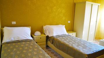 A room with two beds, a small bedside table, a wardrobe, and a wall socket.