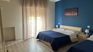 A hotel room with two beds, a cityscape painting, a window with sheer curtains, and patterned floor tiles.
