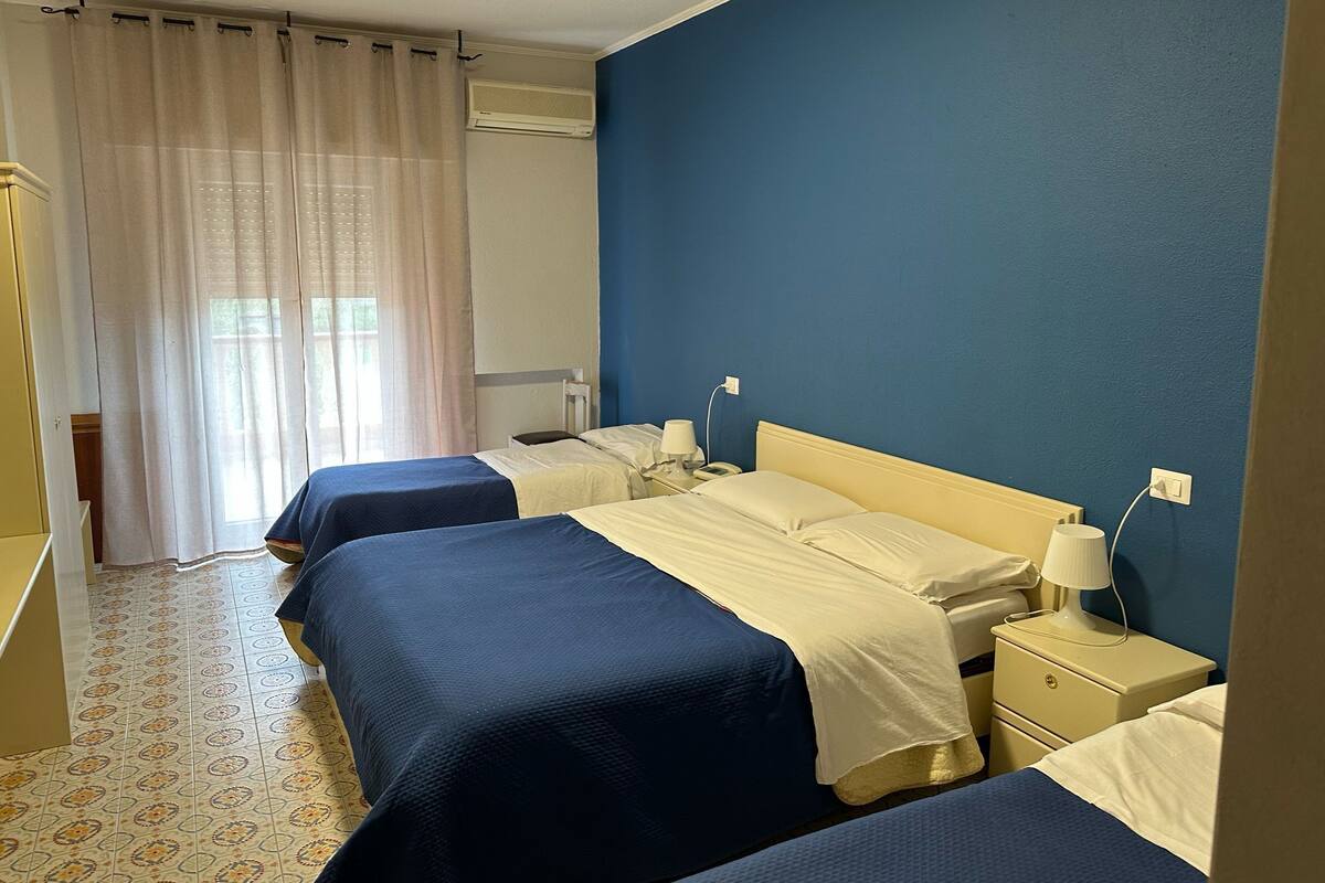 Une chambre d’hôtel avec deux lits, une table de chevet avec une lampe, une commode, une fenêtre avec des rideaux et un appareil de climatisation.