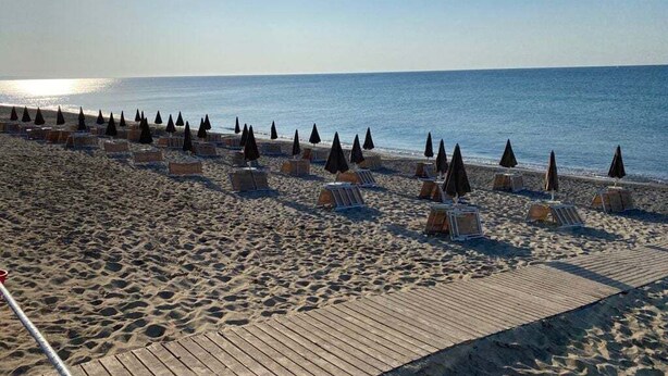 Una playa con filas de tumbonas y sombrillas, un paseo marítimo de madera y el océano al fondo.