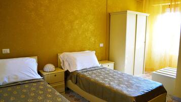 A room with two beds, a wardrobe, and a window with curtains.