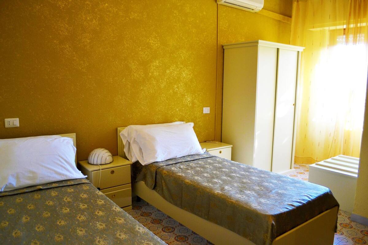 Une chambre avec deux lits, une armoire et une table de chevet avec une lampe.