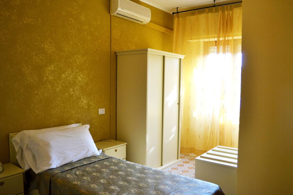 Une chambre avec un lit, une armoire, une table de chevet et une fenêtre avec des rideaux.