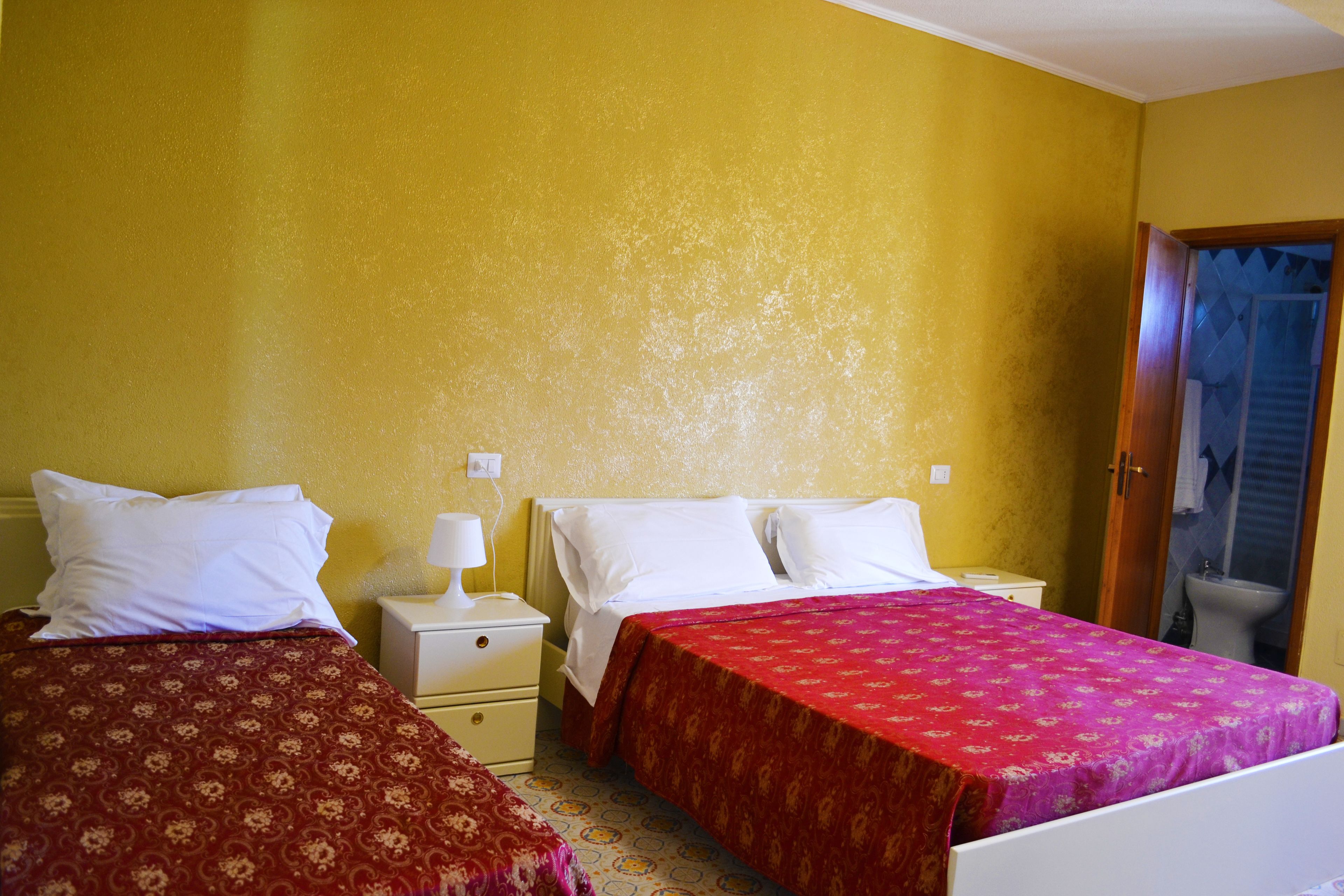 Une chambre avec deux lits, chacun recouvert d’une couvre-lit à motifs différents, une table de chevet avec une lampe et une horloge murale.