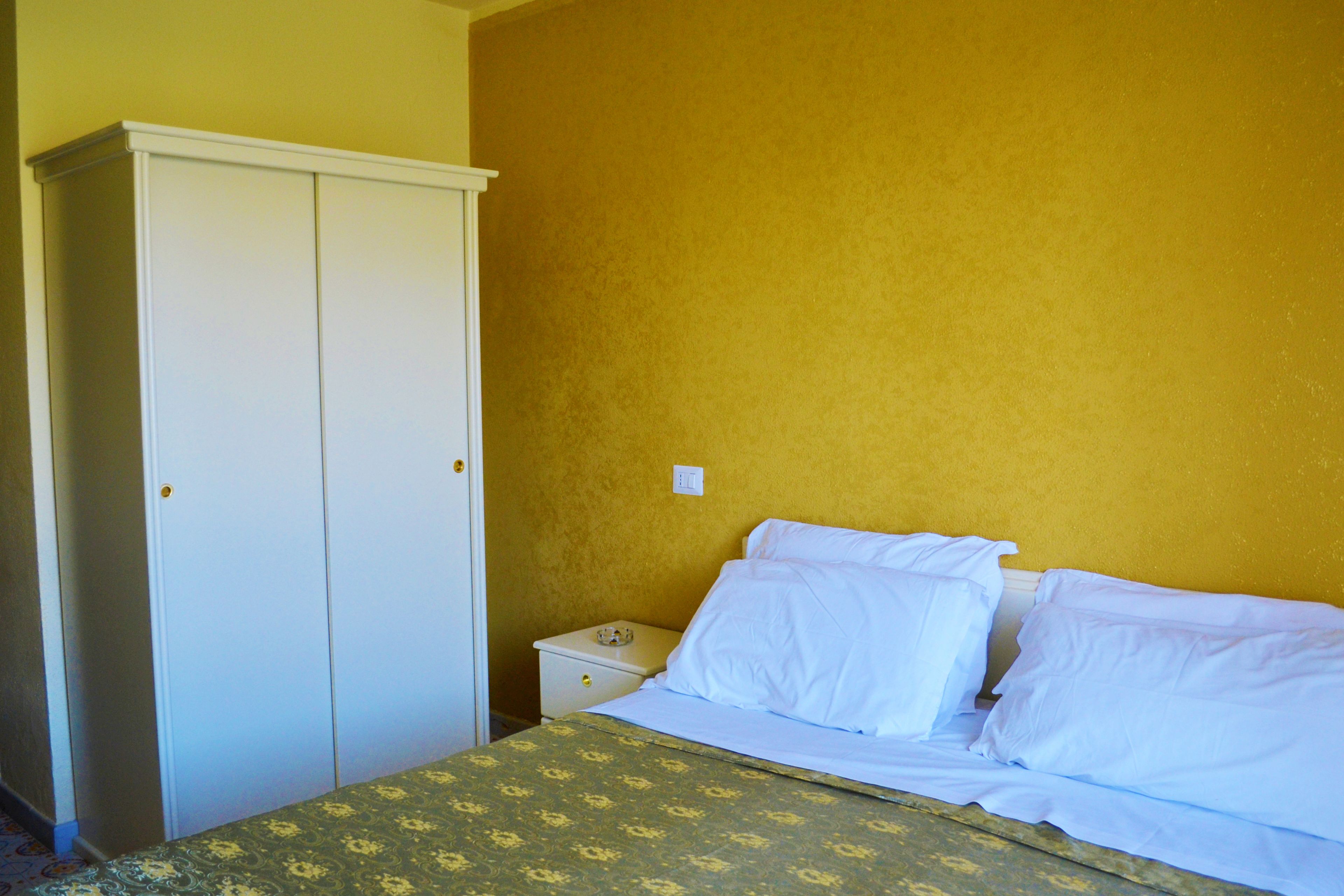 Un dormitorio con una cama, almohadillas blancas, una mesita de noche y un armario.
