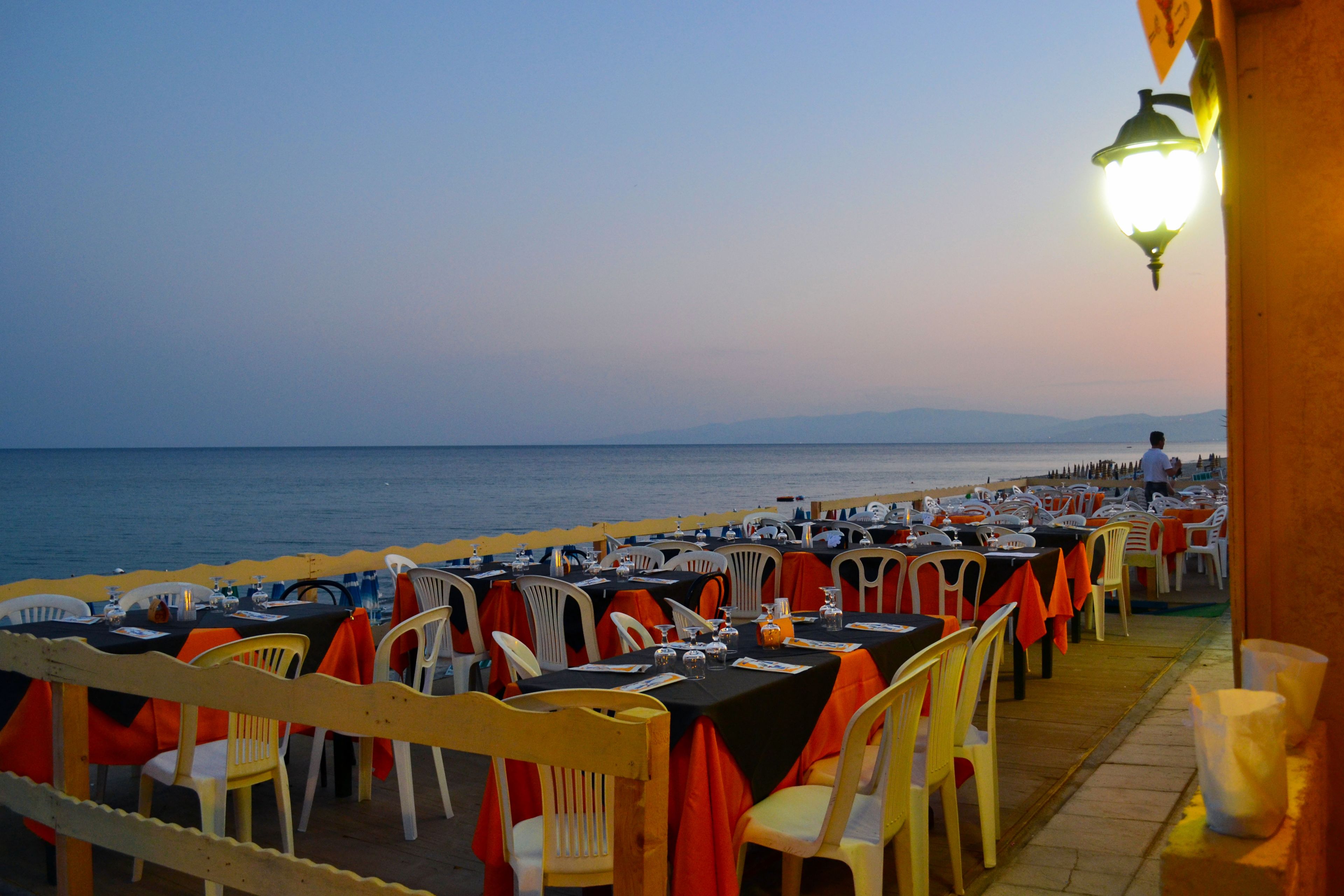 A seaside restaurant with tables set for dining, overlooking the sea.