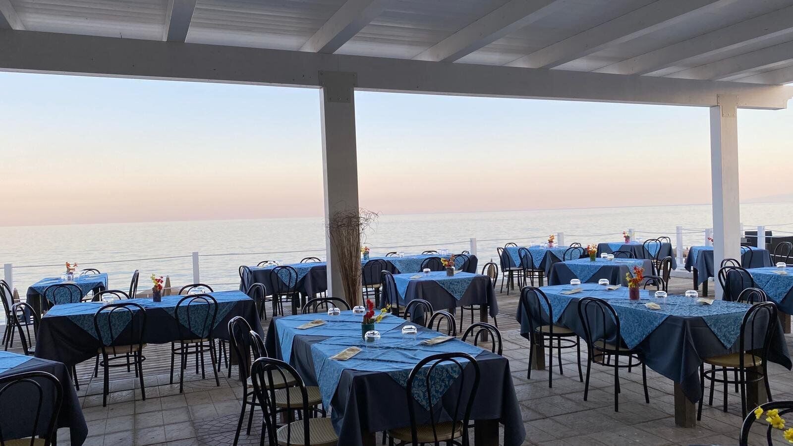 An outdoor dining area with tables set for two, overlooking a body of water.