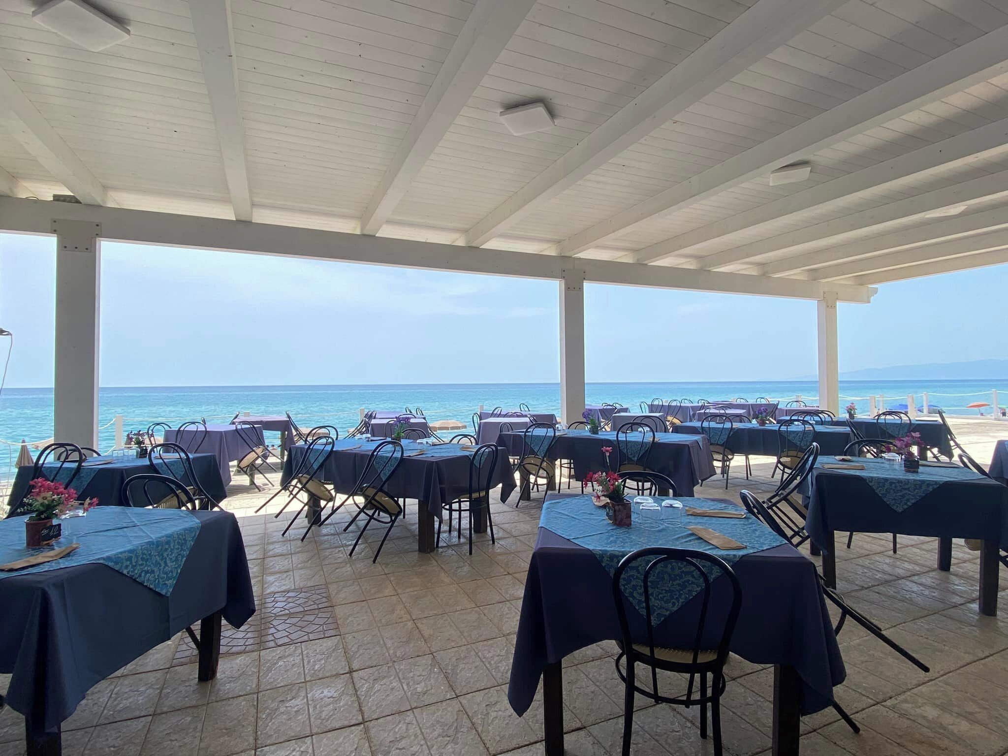 An outdoor dining area with tables and chairs, overlooking the sea.