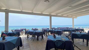 An outdoor dining area with tables and chairs, overlooking the sea.