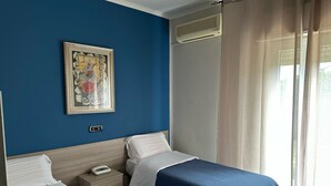 Habitación de hotel con dos camas, una mesita de noche con teléfono, aire acondicionado montado en la pared y una ventana con cortinas.