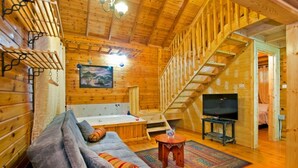 A log cabin interior with a sofa, a bathtub, a TV, and a staircase. - Siesta (Ramot)