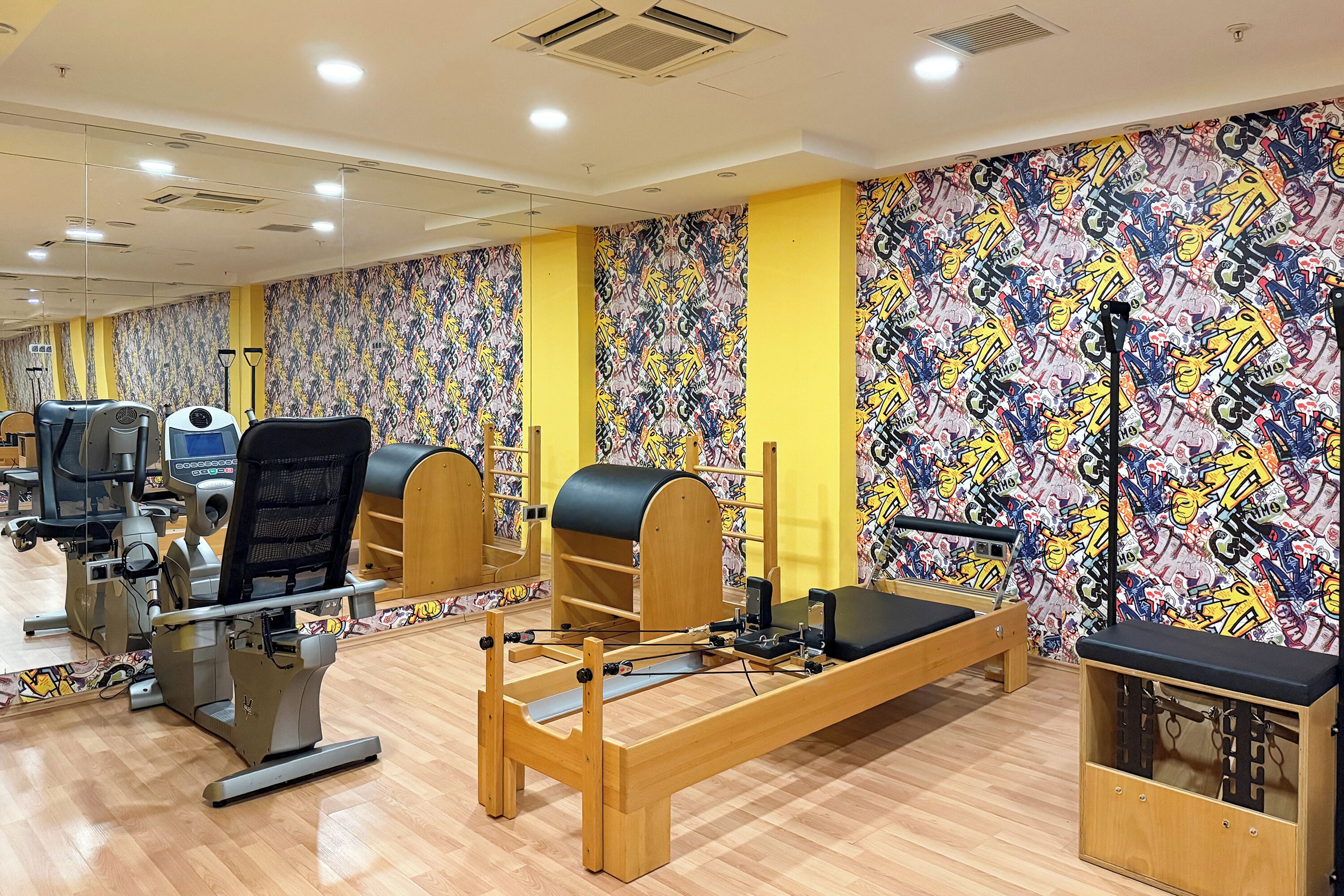 A gym with exercise equipment, mirrored walls, and a graffiti-patterned wall.