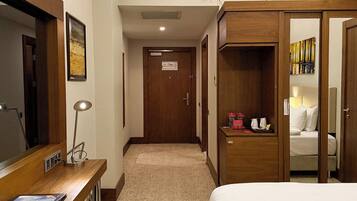 A hotel room with a bed, a desk with a lamp, a wardrobe, and a door leading to another room.