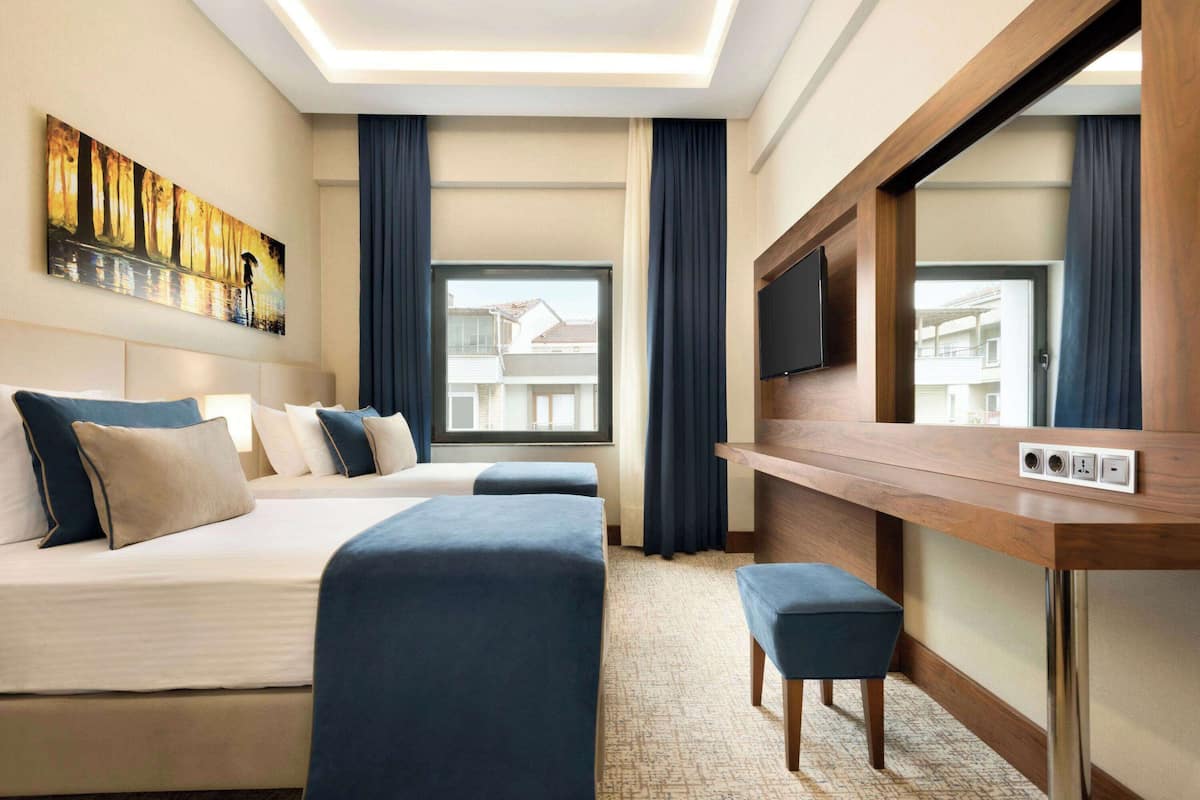 Habitació d'hotel amb un llit gran, una taula de treball amb televisió de pantalla plana, una finestra amb cortines i un quadre al mur.