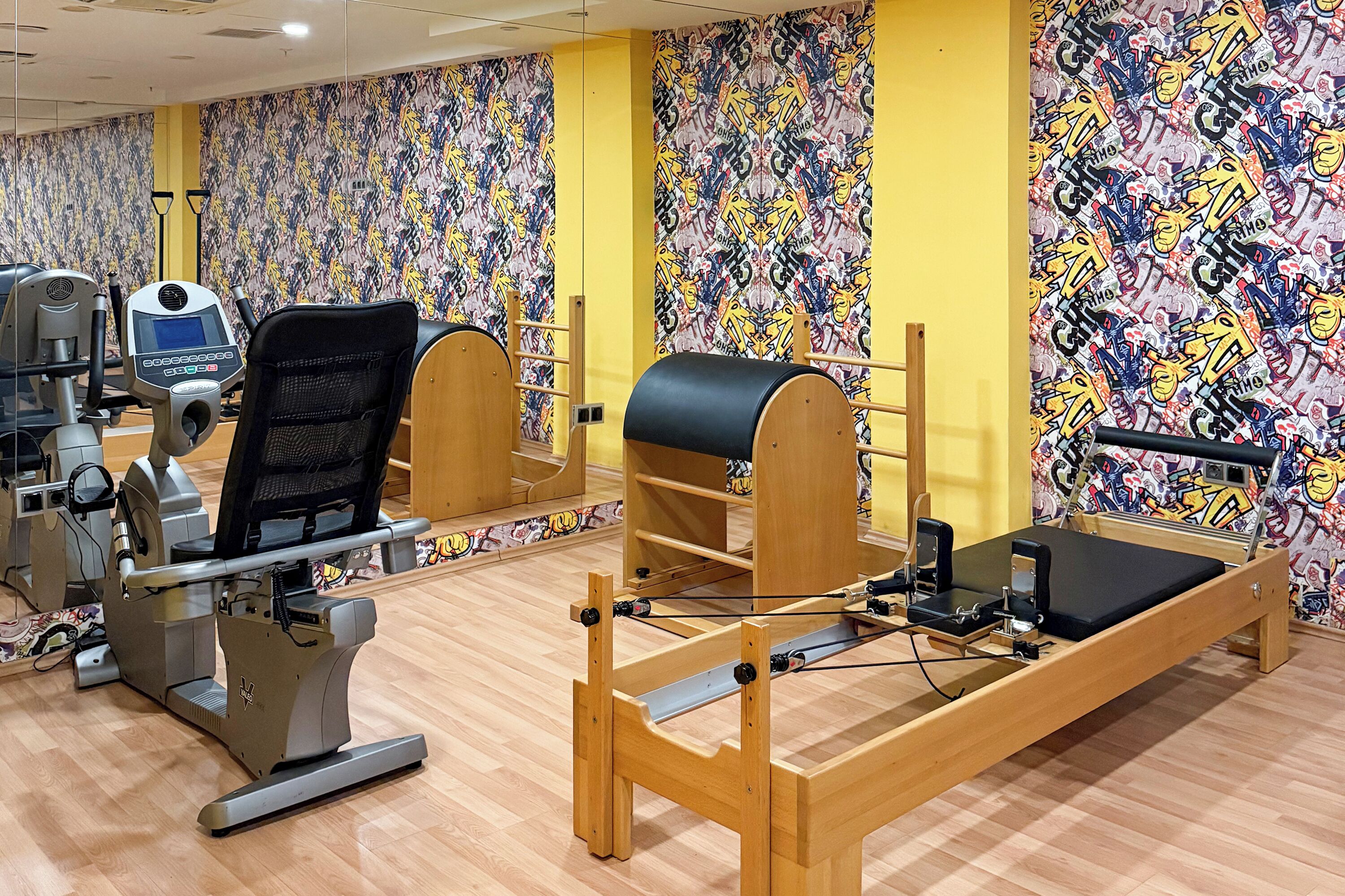 Un gimnasio con equipamiento de ejercicio, un espejo grande y un diseño de pared colorido.