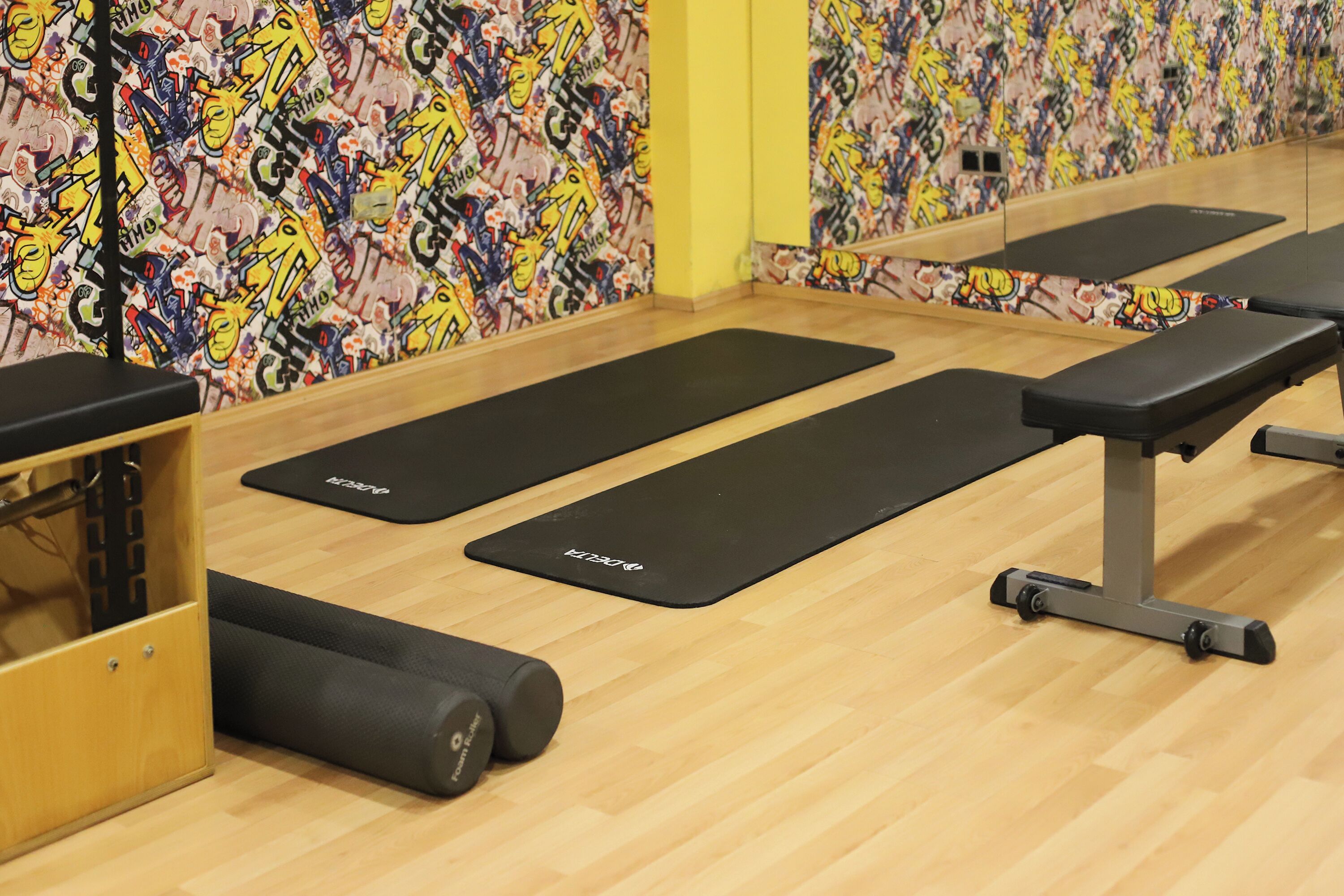 A gym with black mats, wooden flooring, and a mirror on the wall.