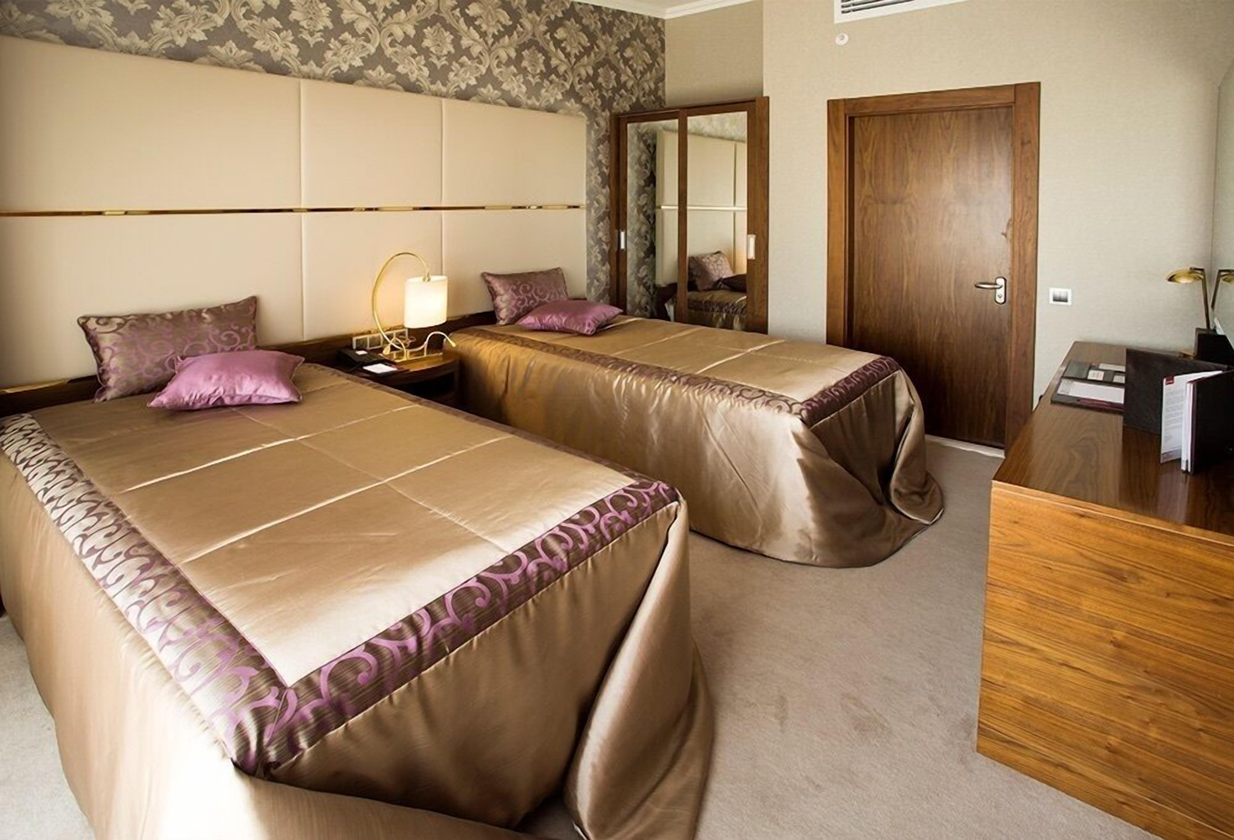 A hotel room with two beds, a wooden desk, a mirror, and a wardrobe.