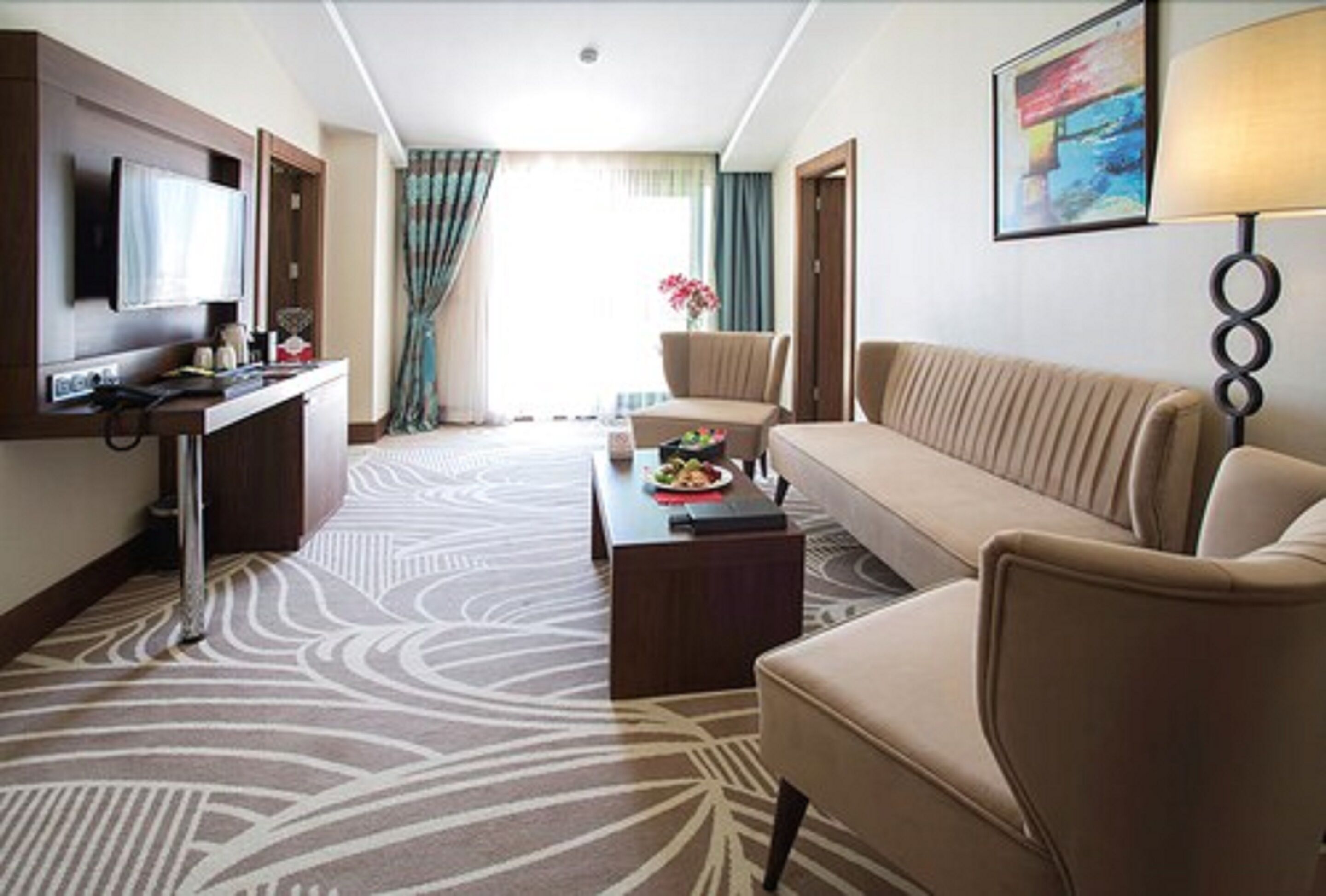 A hotel room with a sofa, armchair, TV, and a small table with a flower vase.