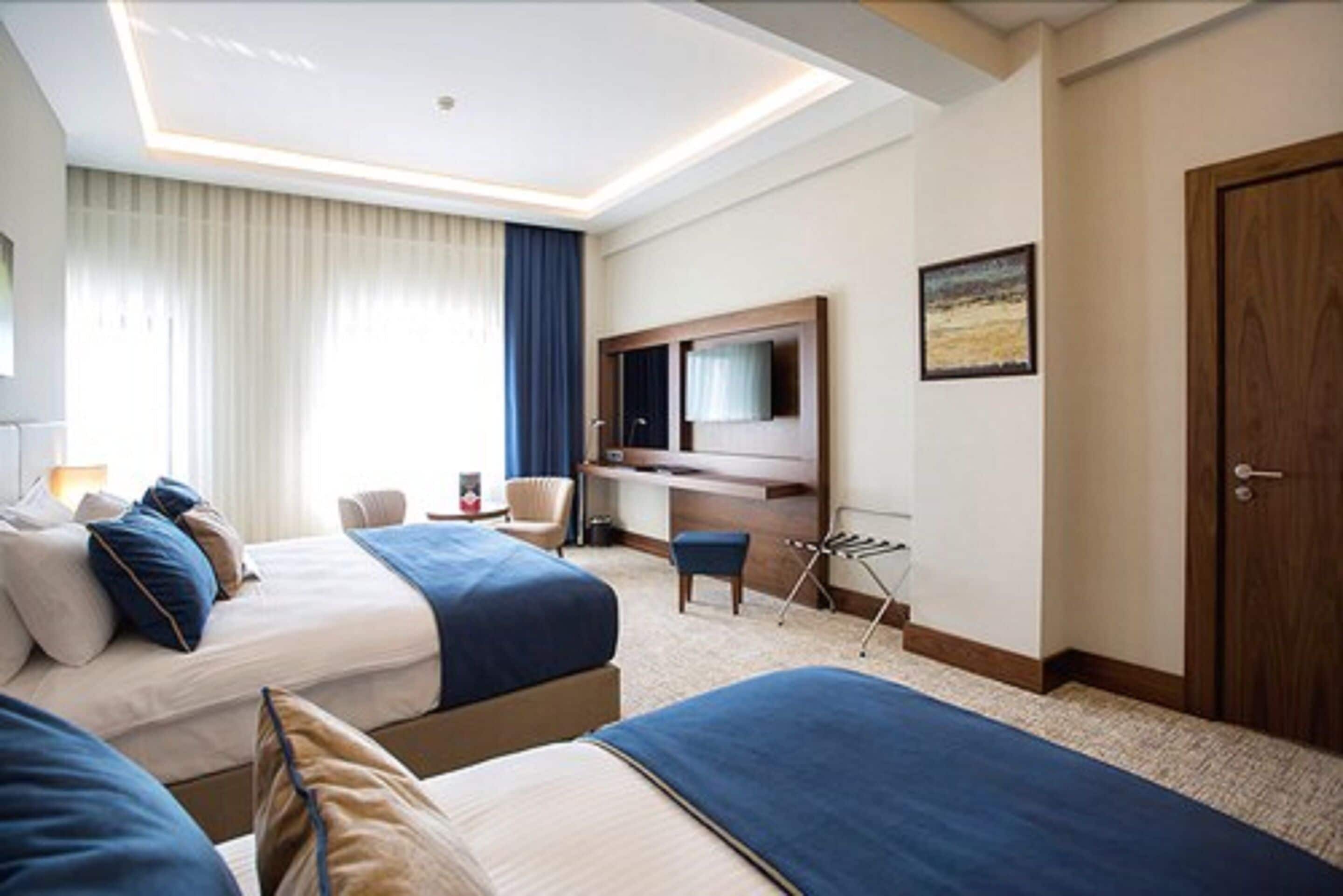 A hotel room with two beds, a desk, a chair, a TV, and a door.
