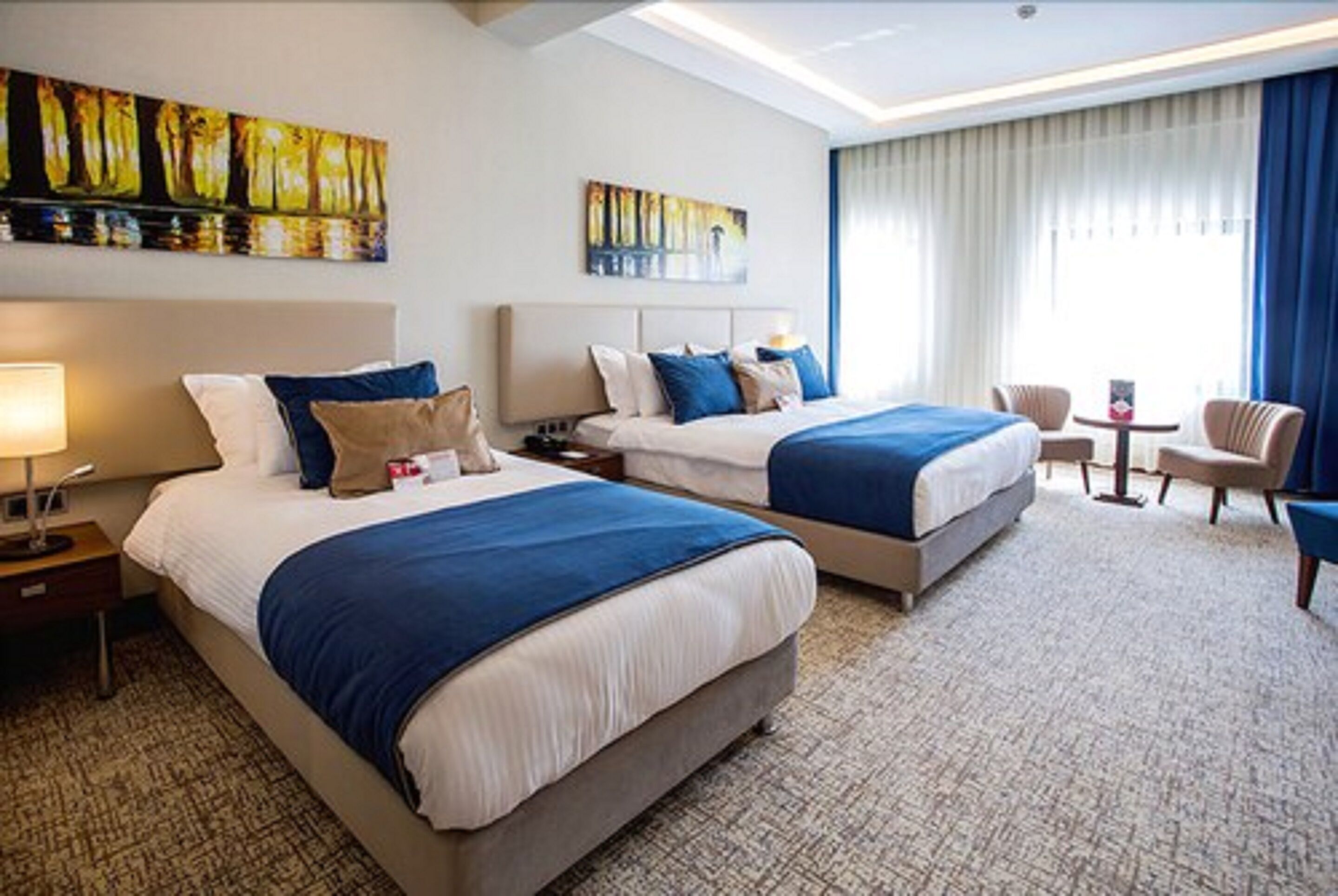 Ein Hotelzimmer mit zwei Betten, einem Schreibtisch, einem Stuhl und Bildern an den Wänden.